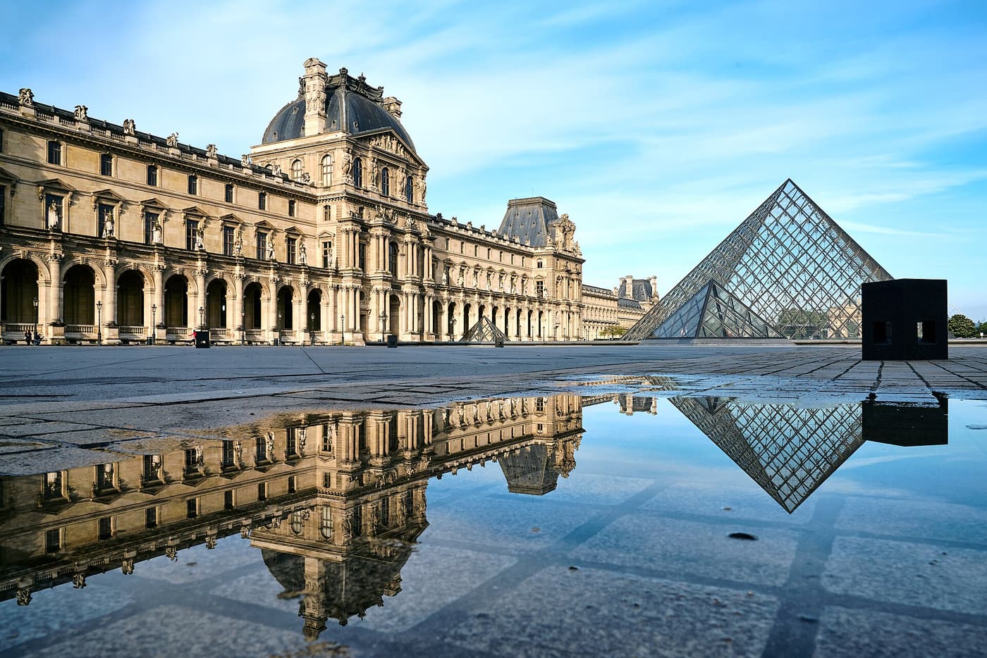The Louvre pyramid and palace reflected in a pool at dawn