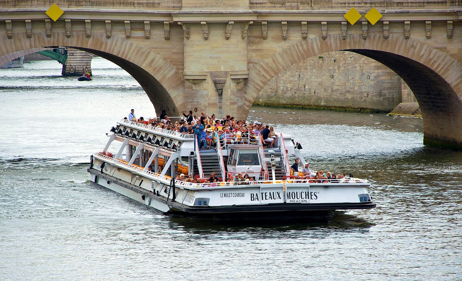 A Seine sightseeing boat passing under a stone bridge in Paris