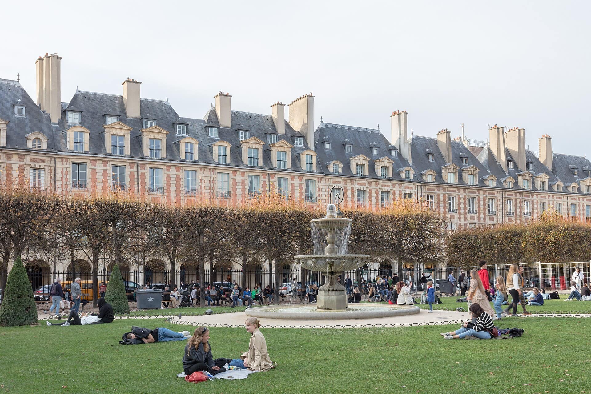 Parisians relaxing on the lawns of the Place des Vosges in front of the fountain and the red-brick houses